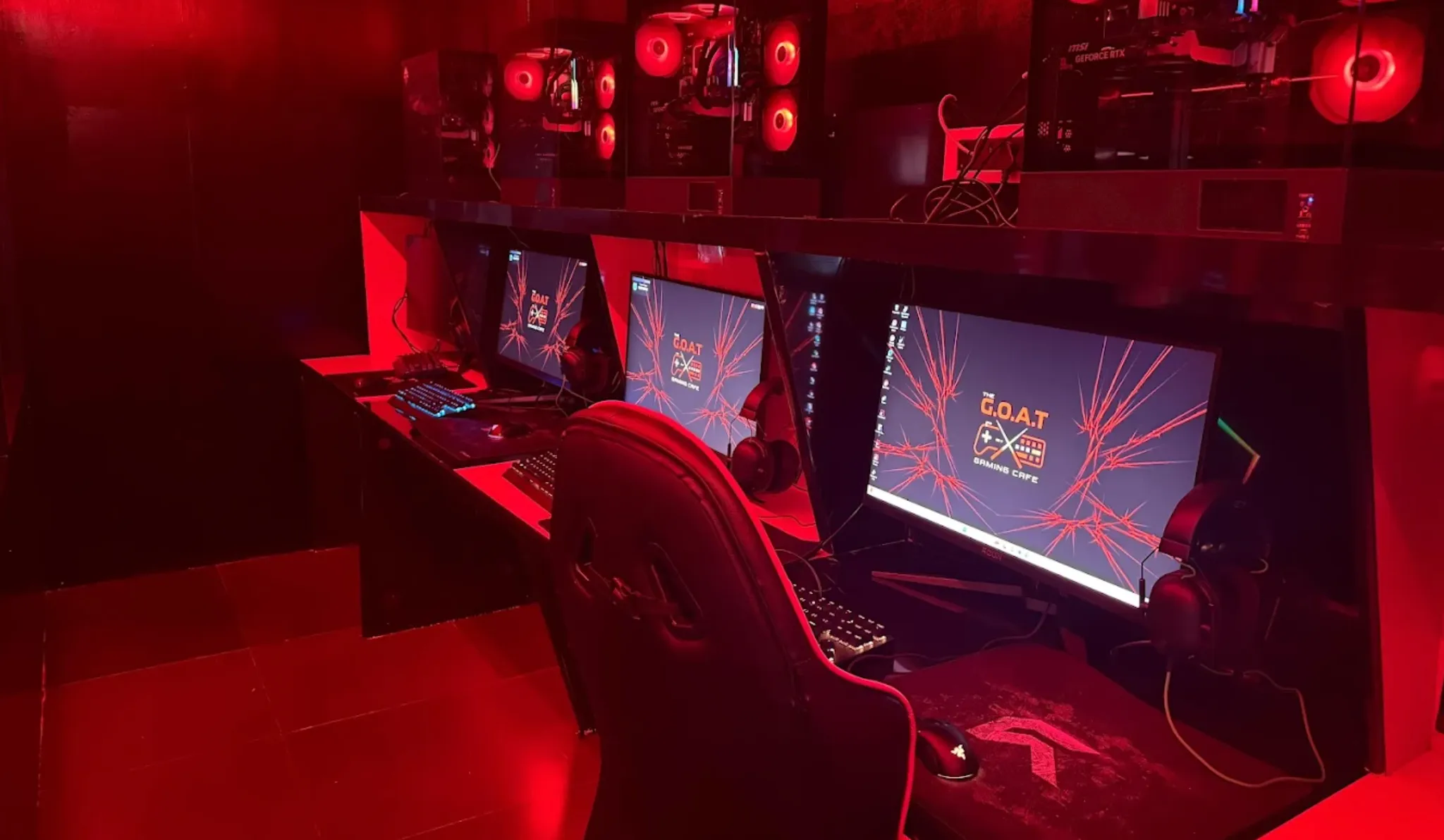 A row of gaming PCs, monitors and chairs under red lighting at the café I visit.